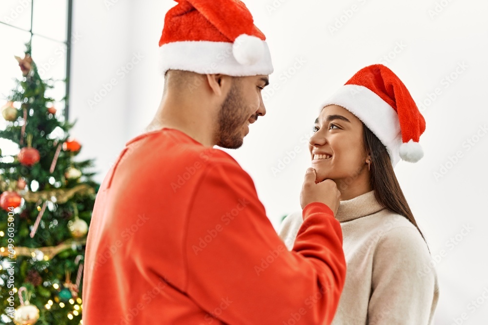 Young latin romantic couple smiling happy hugging and standing by christmas tree at home. Young latin romantic couple smiling happy hugging and standing by christmas tree at home.