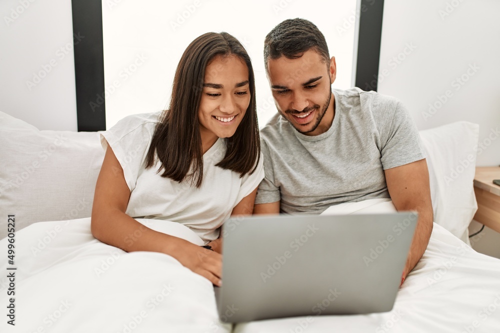 Fototapeta premium Young latin couple smiling happy using laptop at bedroom