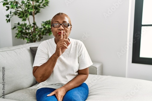 Mature hispanic woman sitting on the sofa at home asking to be quiet with finger on lips. silence and secret concept. © Krakenimages.com