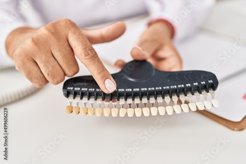 Middle age hispanic woman dentist holding whitening teeth test at clinic