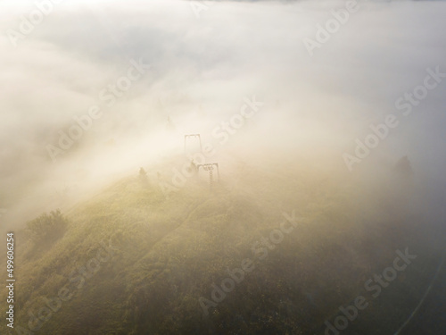 Fog envelops the mountain forest. The rays of the rising sun break through the fog. Aerial drone view.