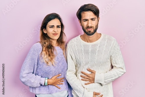 Young hispanic couple wearing casual clothes with hand on stomach because indigestion, painful illness feeling unwell. ache concept.