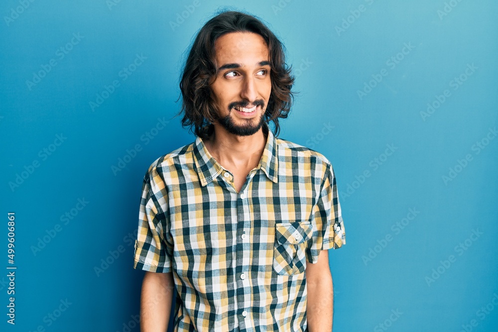 Young hispanic man wearing casual clothes looking away to side with smile on face, natural expression. laughing confident. Young hispanic man wearing casual clothes looking away to side with smile on face, natural expression. laughing confident.