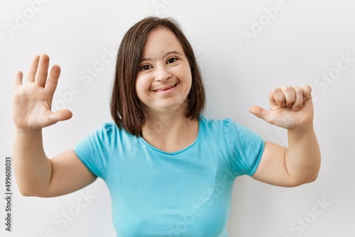 Young down syndrome woman standing over isolated background showing and pointing up with fingers number six while smiling confident and happy. © Krakenimages.com