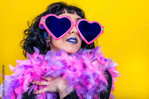 Young woman wears large heart-shaped glasses and a scarf with pink and purple feathers. Beautiful woman has fun at the party. Party concept.