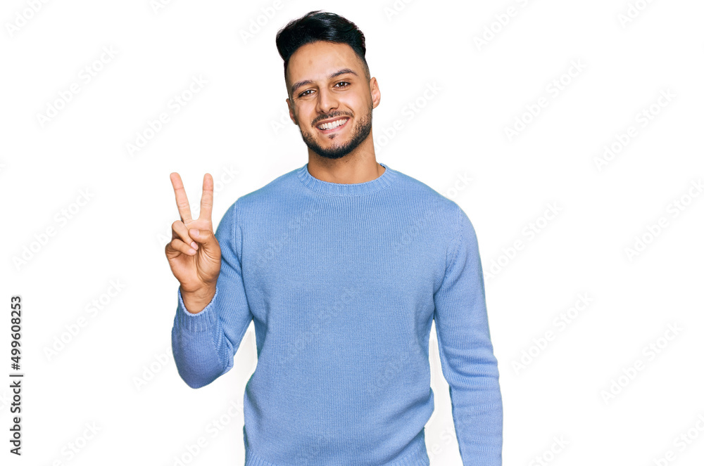 Young arab man wearing casual clothes smiling with happy face winking at the camera doing victory sign. number two. Young arab man wearing casual clothes smiling with happy face winking at the camera doing victory sign. number two.