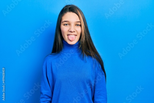 Young brunette girl wearing turtleneck sweater sticking tongue out happy with funny expression. emotion concept.
