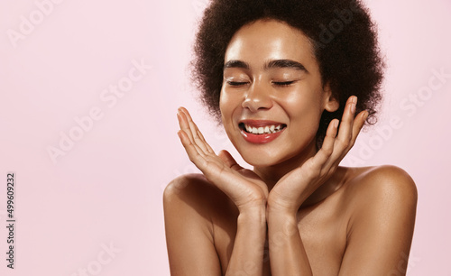 Beauty face and spa. African american woman has clean nourished skin, splash face with water, washing. Girl use antiaging cosmetics and vitamin c serum for better smoother skin tone, pink background