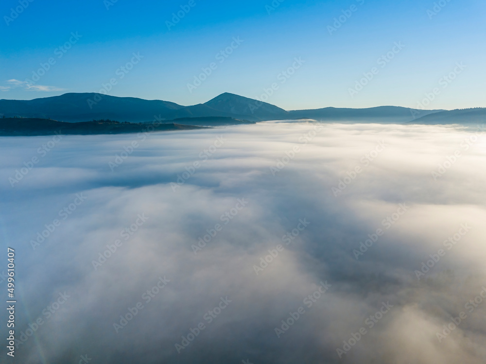 Flight over fog in Ukrainian Carpathians in summer. Mountains on the horizon. A thick layer of fog covers the mountains with a continuous carpet. Aerial drone view.