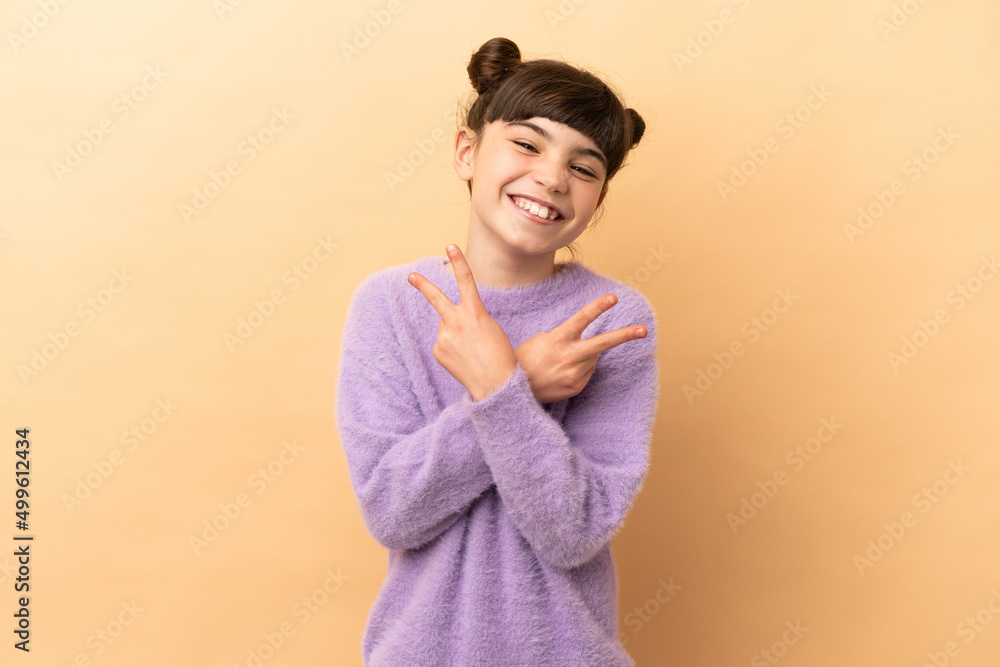 Little caucasian girl isolated on beige background smiling and showing victory sign Little caucasian girl isolated on beige background smiling and showing victory sign