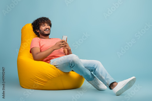 Happy eastern guy chilling at bean bag with smartphone