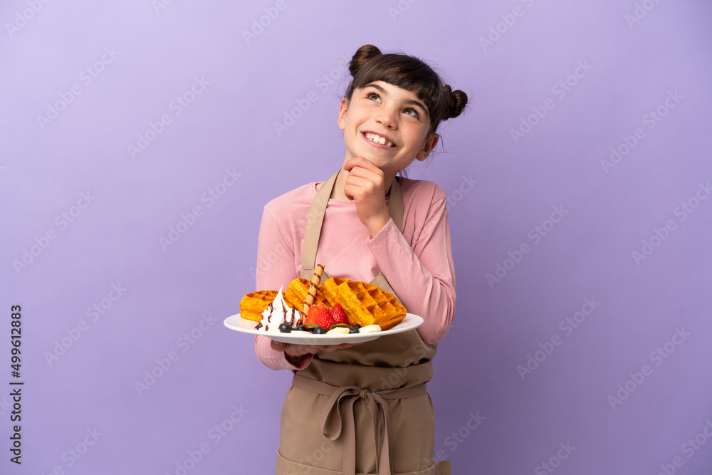 Little caucasian girl holding waffles isolated on purple background and looking up Little caucasian girl holding waffles isolated on purple background and looking up