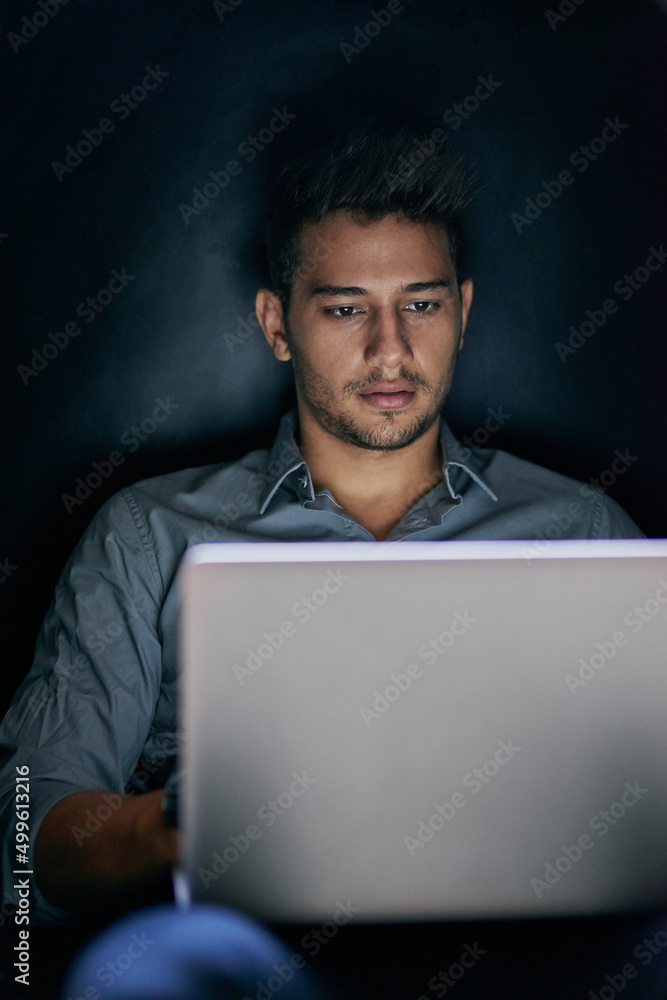 Working in the dark. Shot of a focused young man working on his laptop at night time. Working in the dark. Shot of a focused young man working on his laptop at night time.