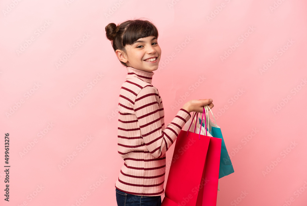 Little caucasian girl isolated on pink background holding shopping bags and smiling