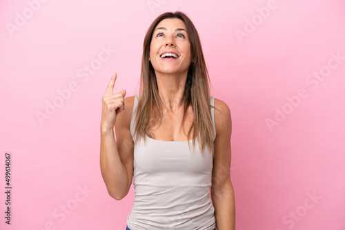 Middle age caucasian woman isolated on pink background pointing up and surprised