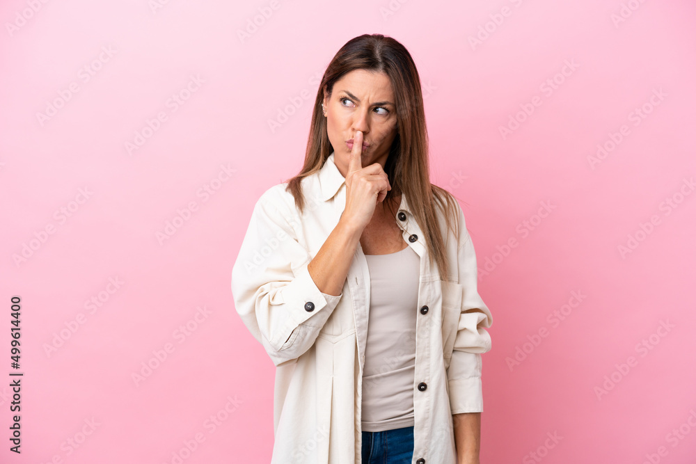 Middle age caucasian woman isolated on pink background showing a sign of silence gesture putting finger in mouth Middle age caucasian woman isolated on pink background showing a sign of silence gesture putting finger in mouth