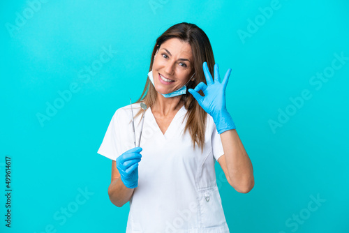 Middle age doctor woman isolated on blue background showing ok sign with fingers