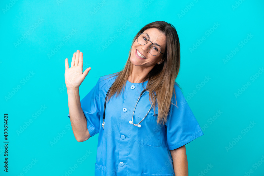 Middle age surgeon woman isolated on blue background saluting with hand with happy expression Middle age surgeon woman isolated on blue background saluting with hand with happy expression