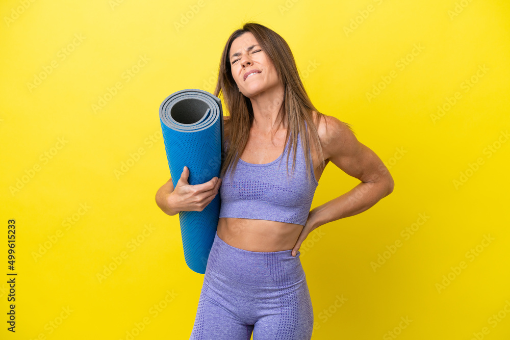 Sport woman going to yoga classes while holding a mat isolated non yellow background suffering from backache for having made an effort Sport woman going to yoga classes while holding a mat isolated non yellow background suffering from backache for having made an effort