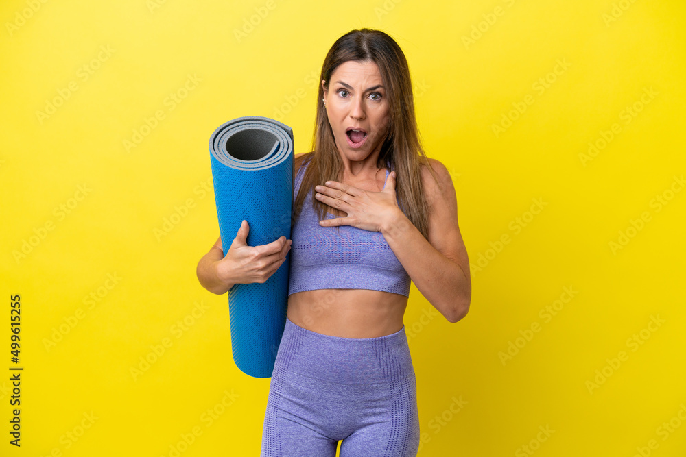 Sport woman going to yoga classes while holding a mat isolated non yellow background surprised and shocked while looking right Sport woman going to yoga classes while holding a mat isolated non yellow background surprised and shocked while looking right