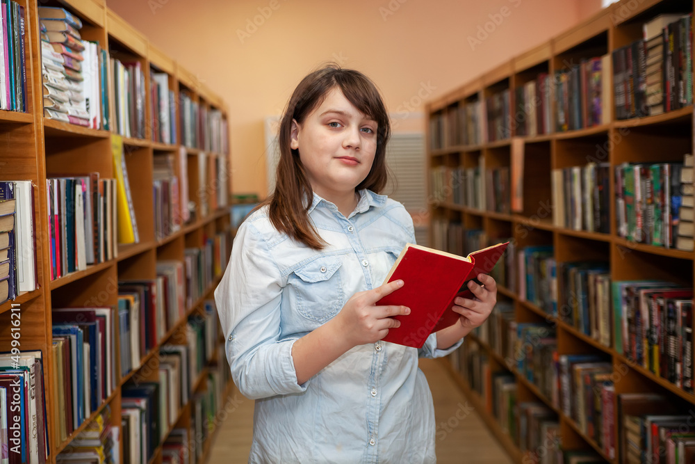 Happy schoolgirl reading a book in the library at school Happy schoolgirl reading a book in the library at school