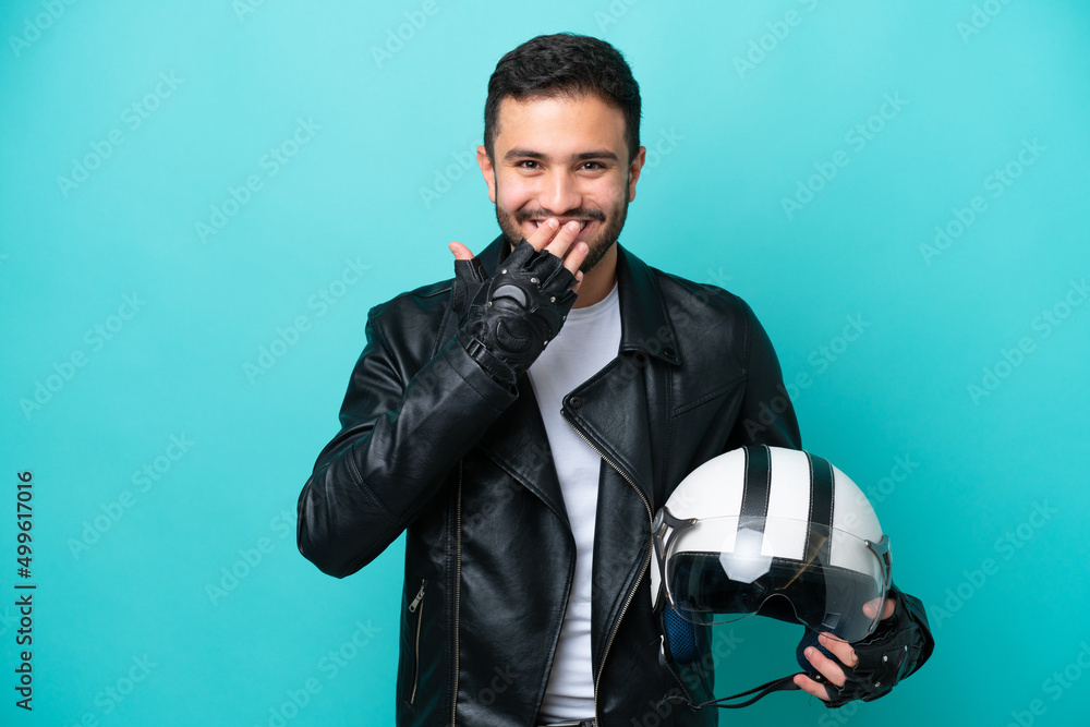 Young Brazilian woman with a motorcycle helmet isolated on blue background happy and smiling covering mouth with hand Young Brazilian woman with a motorcycle helmet isolated on blue background happy and smiling covering mouth with hand