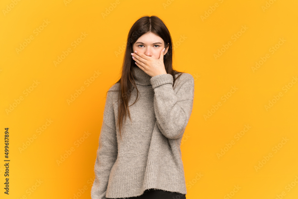 Young Ukrainian girl isolated on yellow background covering mouth with hand Young Ukrainian girl isolated on yellow background covering mouth with hand
