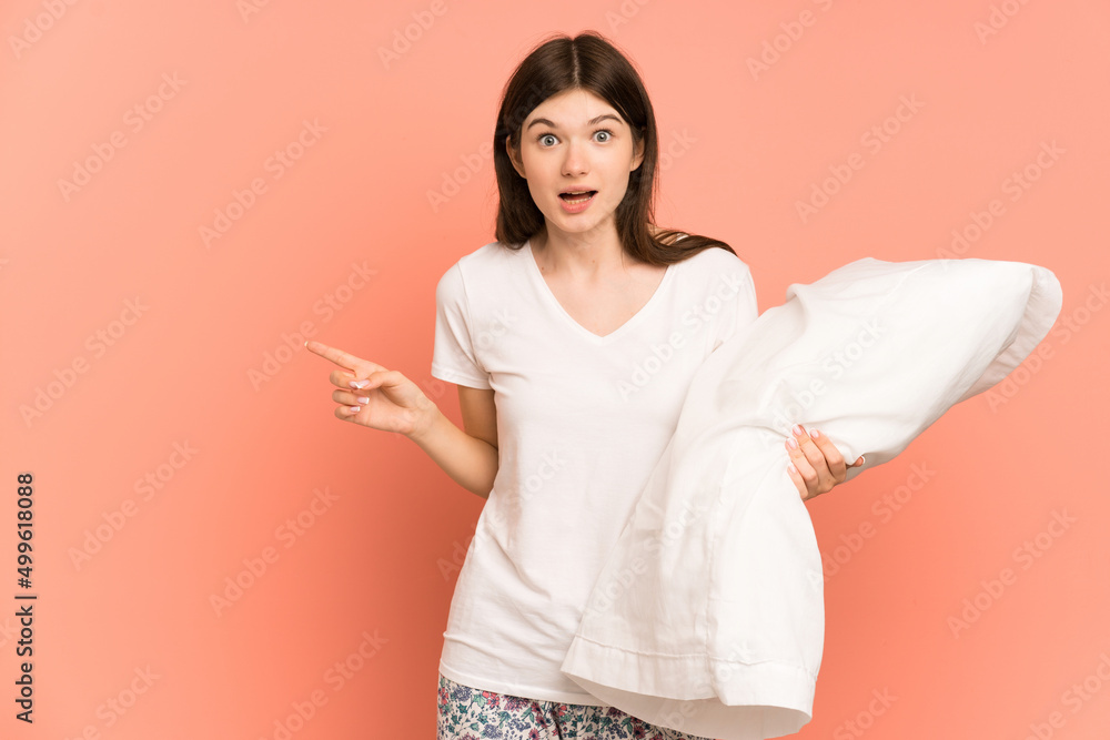 Young Ukrainian girl isolated on pink background in pajamas and surprised while pointing finger to the side Young Ukrainian girl isolated on pink background in pajamas and surprised while pointing finger to the side