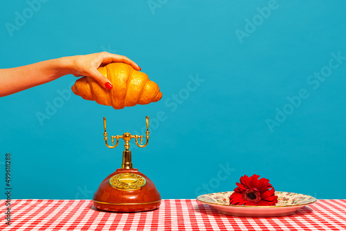 Fotografia Female hand tasting crispy croissant on plaid tablecloth isolated on bright blue background