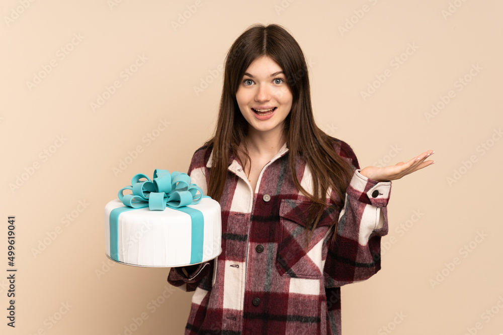 Young Ukrainian girl holding a big cake isolated on beige background with shocked facial expression Young Ukrainian girl holding a big cake isolated on beige background with shocked facial expression