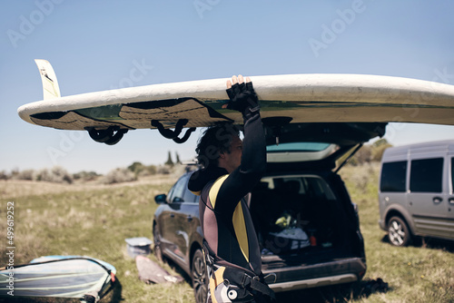 Windsurfer packing and unpacking sports equipment from a car in nature.