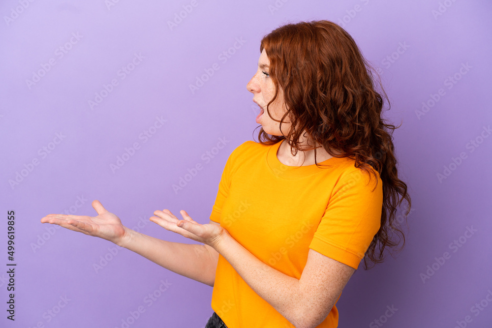 Teenager redhead girl over isolated purple background with surprise expression while looking side Teenager redhead girl over isolated purple background with surprise expression while looking side
