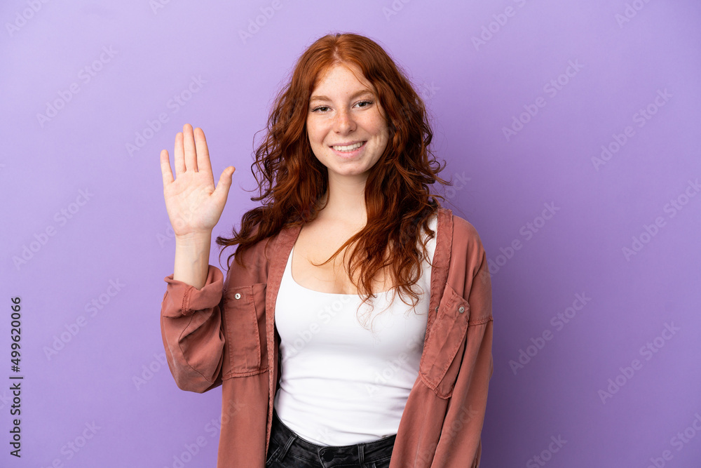 Teenager redhead girl over isolated purple background saluting with hand with happy expression Teenager redhead girl over isolated purple background saluting with hand with happy expression