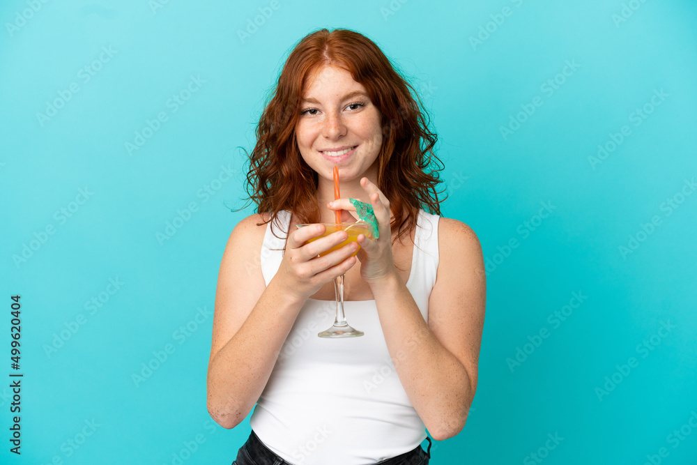 Teenager redhead girl isolated on blue background in swimsuit and holding a cocktail Teenager redhead girl isolated on blue background in swimsuit and holding a cocktail