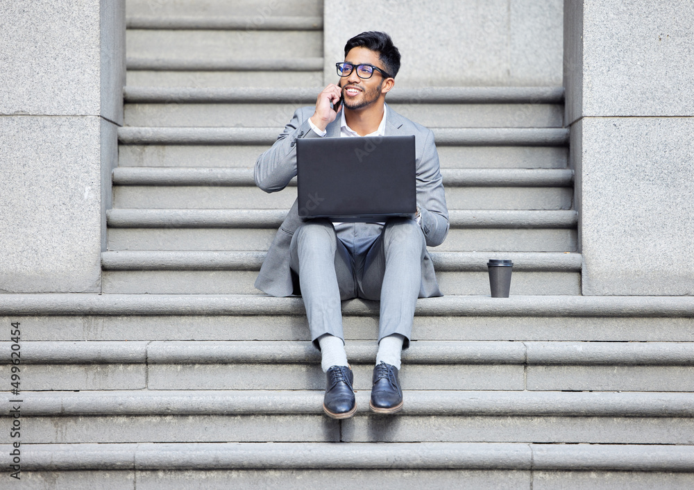 Another successful business call. Shot of a young businessman using a laptop while on the phone in the city. Another successful business call. Shot of a young businessman using a laptop while on the phone in the city.