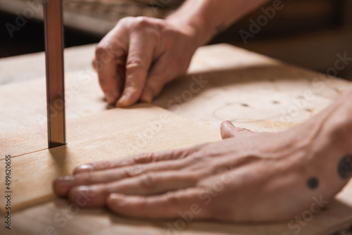 cropped view of blurred carpenter cutting plywood with band saw.