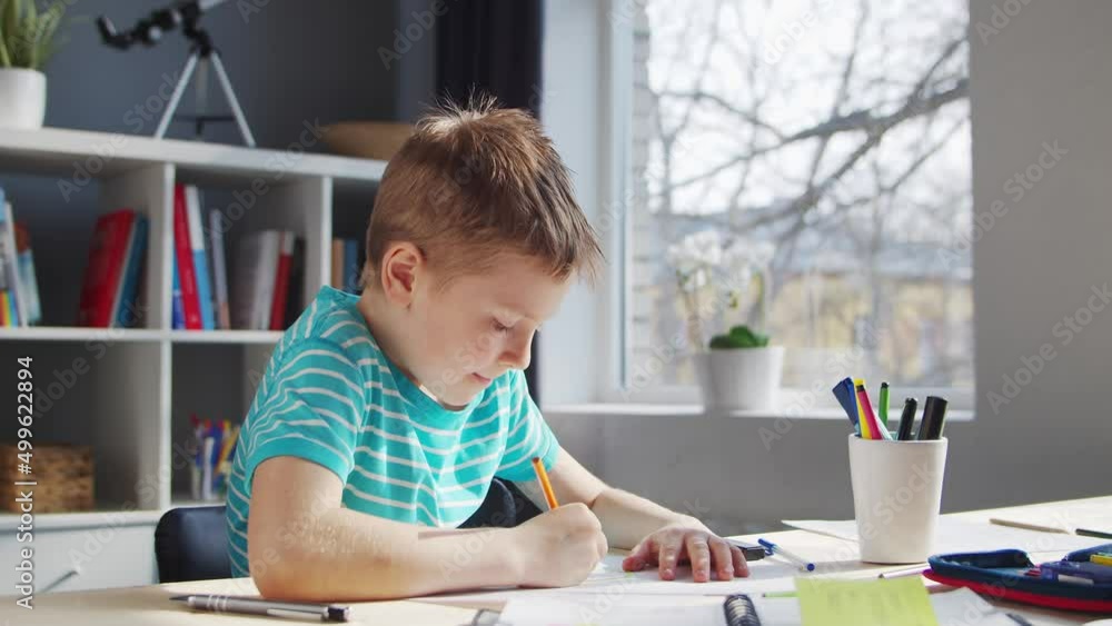 Boy is Doing his Homework at the Table. Cute Child is Learning at Home with the Help of Textbooks and School Materials. Study and Education Concept. Boy is Doing his Homework at the Table. Cute Child is Learning at Home with the Help of Textbooks and School Materials. Study and Education Concept.