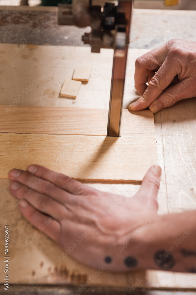 cropped view of joiner cutting plywood with band saw. cropped view of joiner cutting plywood with band saw.