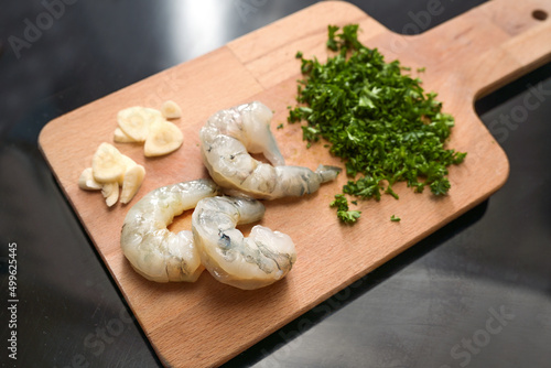 Raw peeled shrimps with garlic and chopped parsley on a wooden kitchen board, ingredients for a delicious tapa appetizer, copy space, selected focus