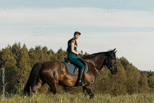 Teenage girl riding bay horse in field.