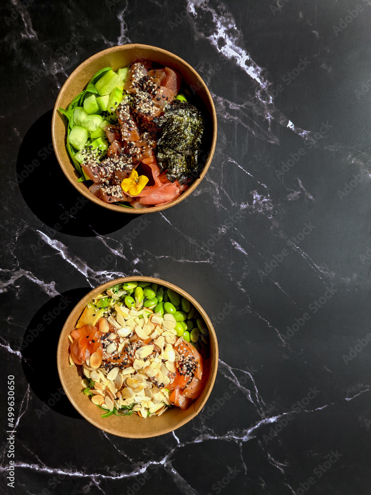 Top view of wok box, bowl of rice on background. Rice fried and stirred with salmon, avocado, onion, cucumber, broccoli, sesame. Chinese, Asian food delivery. Packaging for woks. 