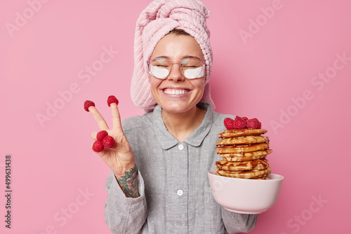 Foto Positive young woman has fun going to eat yummy pancakes with raspberries and ho