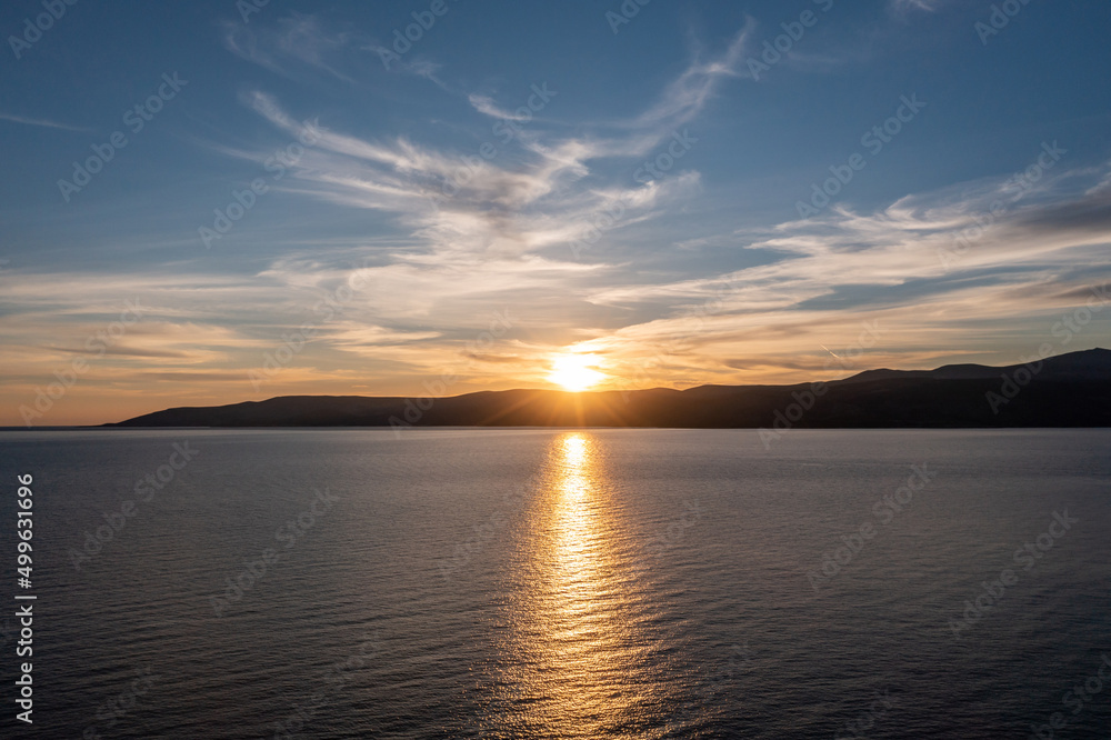 Sunset over Koufonisia island silhouette, Cyclades, Greece. Sunbeam paints gold Aegean calm sea.