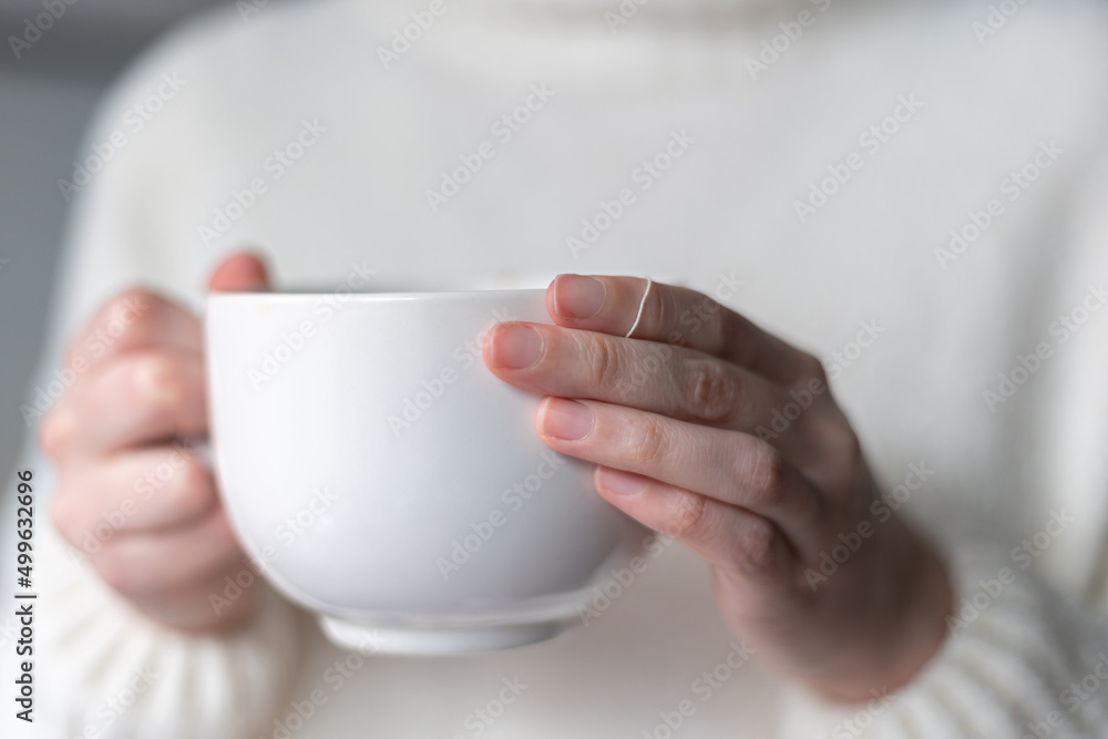 close up of woman's hands holding a big white cup of hot tea close up of woman's hands holding a big white cup of hot tea