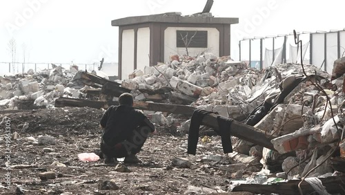 An unrecognizable refugee, with his back to the camera is shaving while crouching, in an abandoned temporary refugee camp. he is holding a tiny mirror in one hand. Belgrade, Serbia. photo