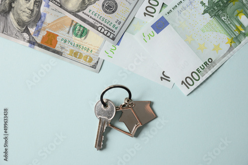 Key for a new house or apartment and currency paper banknotes euro dollars bills on blue background. View from above. Concept expensive utility bills and house payments. photo