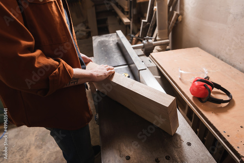 cropped view of woodworker holding board near jointer machine.