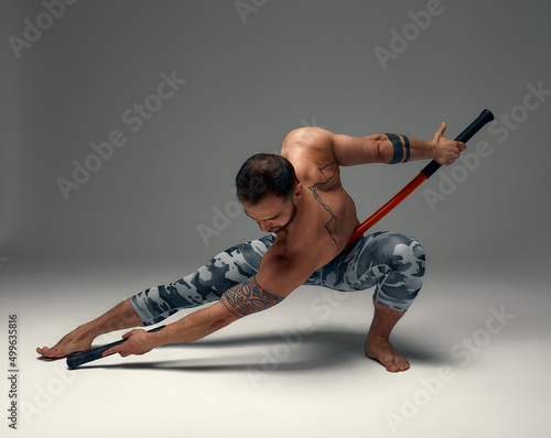 A ninja man holds on to a fighting stick and attacks close-up on gray studio background photo