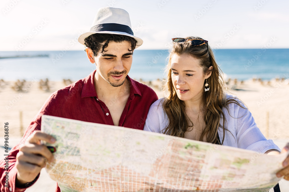 Traveler couple looking for direction on map while enjoying their summer holidays together at the beach. Travel and relationship concept.