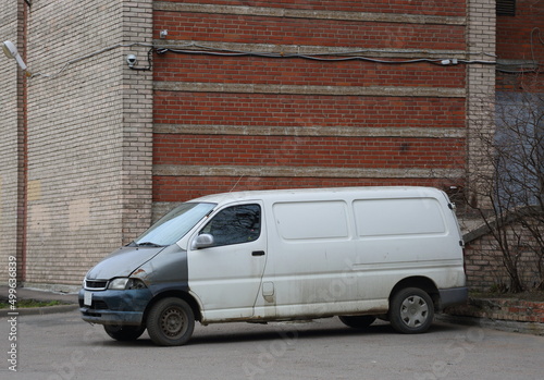 Old rusty white minivan parked at a brick house walls, Kollontai Street, St. Petersburg, Russia, April 2022